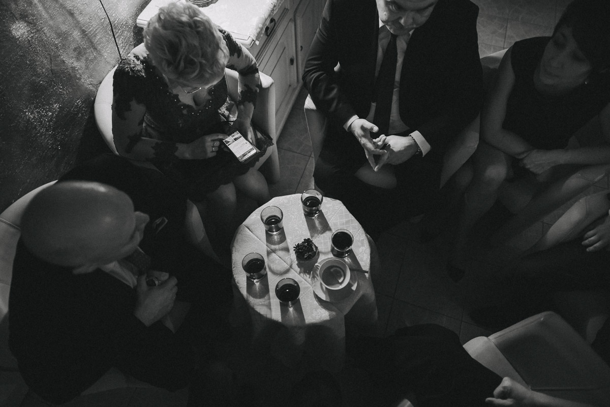Szklanki z alkoholem stojące na małym okrągłym stoliku, wokół którego siedzą ludzie.