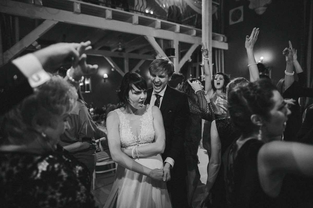 Pani młoda tańczy z gościem pośród innych gości podczas przyjęcia weselnego.