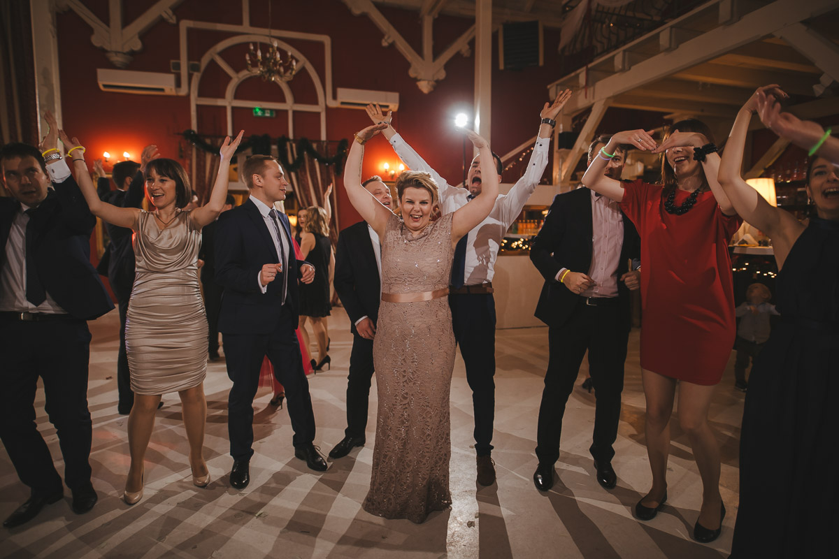 Goście weselni podczas tańca podnoszą ręce w górę.
