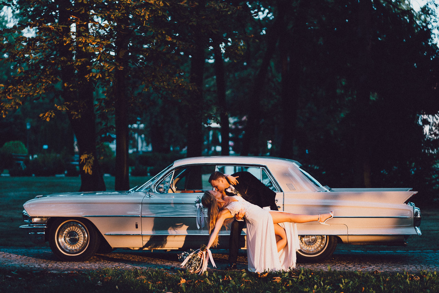 Para młoda całuje się na tle weselnego samochodu. Pytania do fotografa