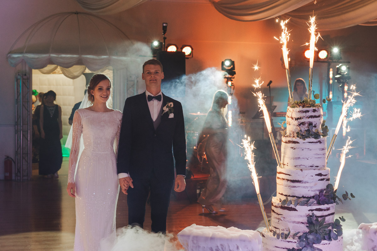 Para młoda patrzy na oświetlony fajerwerkami tort weselny w Hotelu Maxim Stawiszyn.