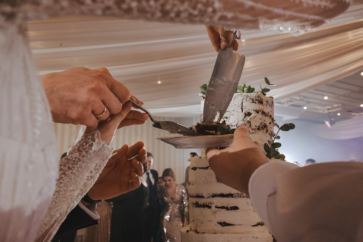 Hotel Maxim Stawiszyn-Państwo młodzi kroją tort weselny, a mężczyzna trzyma w ręce talerz.