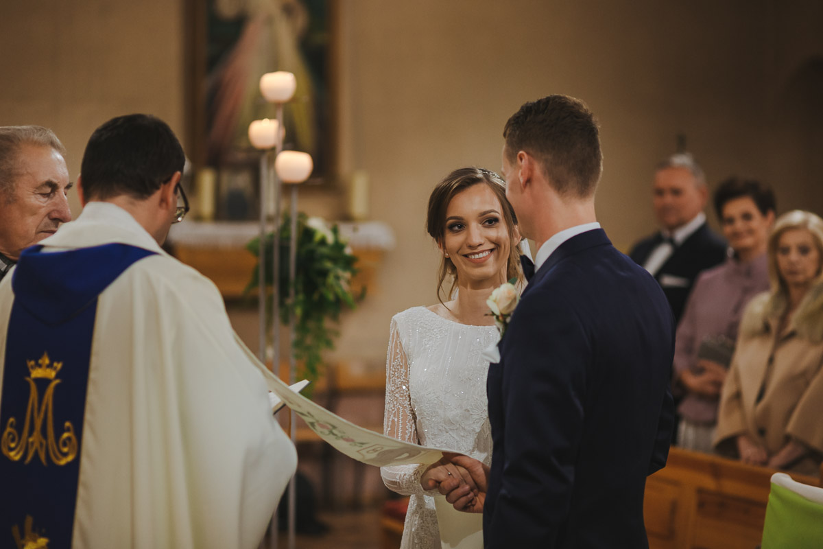 Para młoda trzymająca się za ręce podczas przysięgi małżeńskiej.