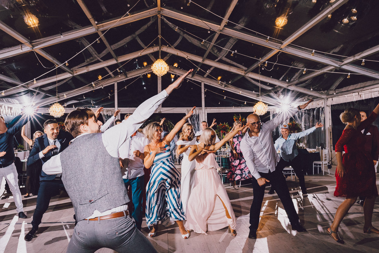 Goście podczas zabawy na przyjęciu weselnym podnoszą ręce w górę.