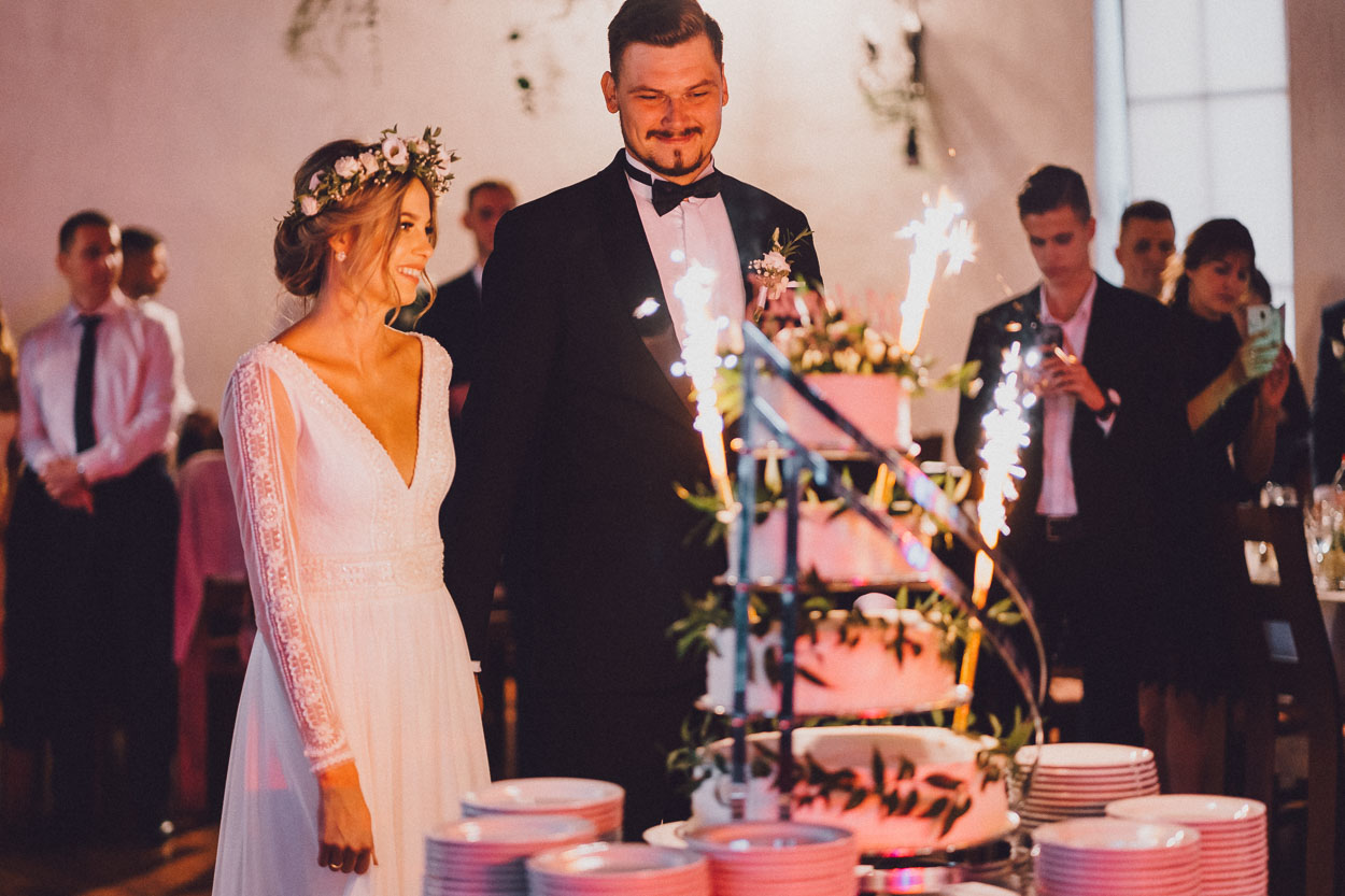Nowożeńcy stojąc obok siebie patrzą na tort weselny w Chacie Baranowskiej.