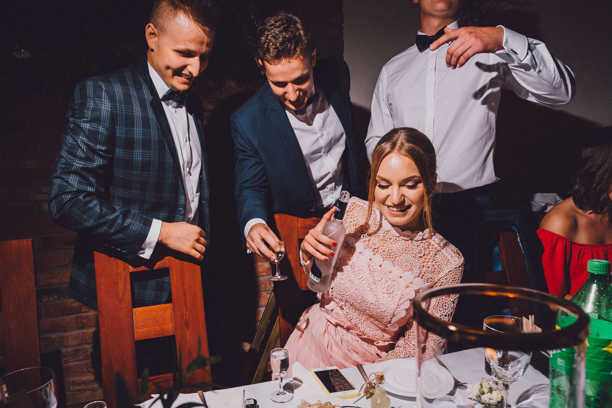 Chata Baranowska-kobieta siedzi przy stoliku z butelką w ręce, mężczyźni stoją za nią.