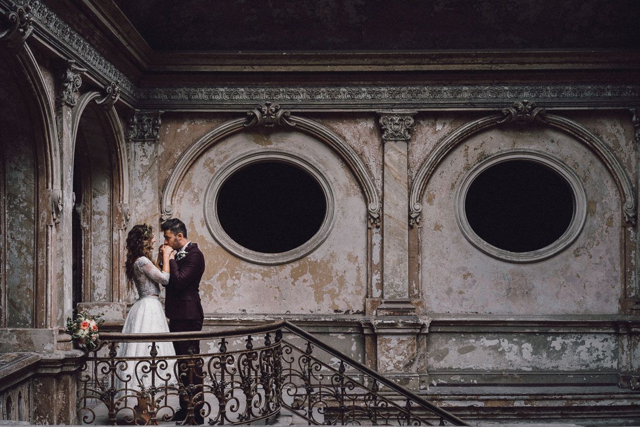 Pan młody całuje w dłonie żonę stojąc na balkonie we wnętrzach Pałacu Karowiarki
