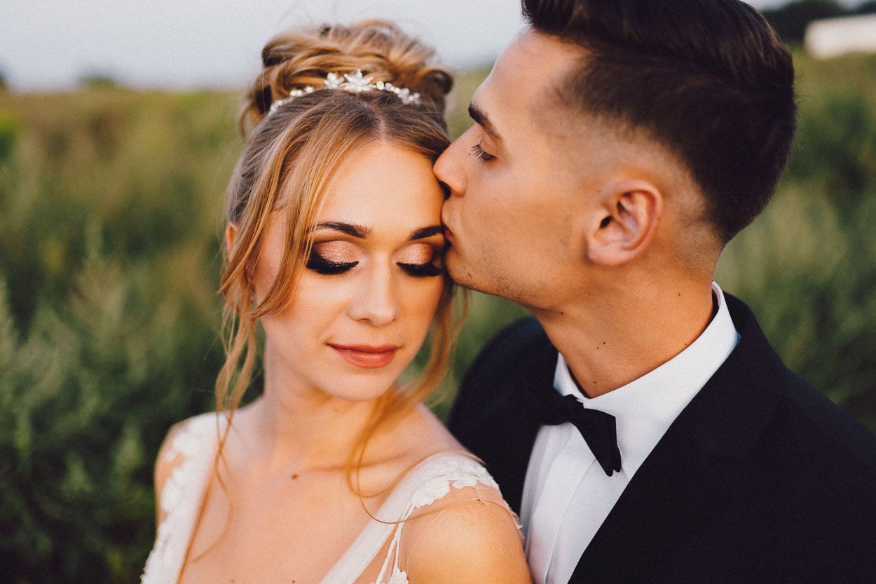 Pan młody całuje żonę na sesji ślubnej w plenerze w dniu ślubu