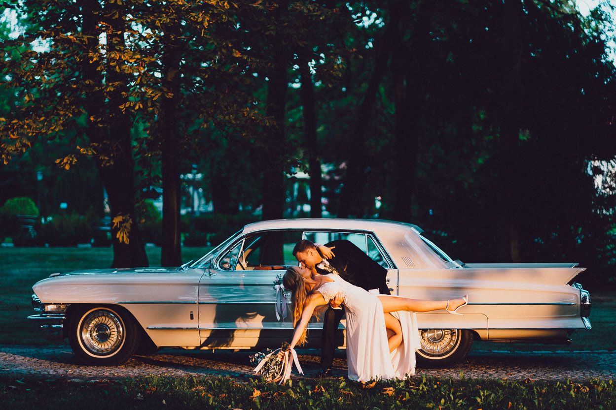 Para młoda całująca się na tle samochodu ślubnego